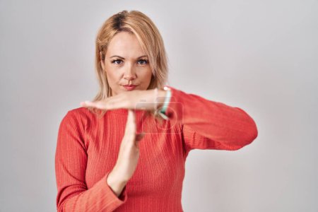 Photo for Blonde woman standing over isolated background doing time out gesture with hands, frustrated and serious face - Royalty Free Image