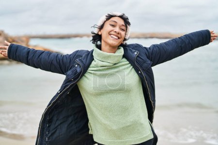 Téléchargez les photos : Jeune belle femme hispanique souriante confiante debout avec les bras ouverts au bord de la mer - en image libre de droit