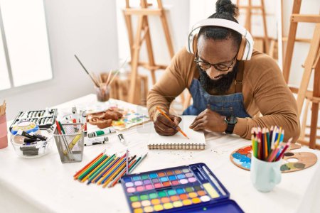 Foto de Young african american artist man using headphones drawing at art studio. - Imagen libre de derechos