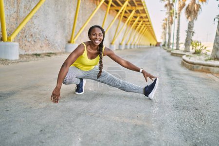 Téléchargez les photos : Femme afro-américaine portant des vêtements de sport étirant la jambe dans la rue - en image libre de droit