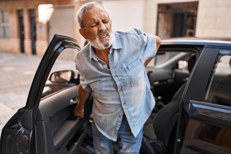 Téléchargez les photos : Homme âgé aux cheveux gris souffrant de maux de dos debout en voiture dans la rue - en image libre de droit