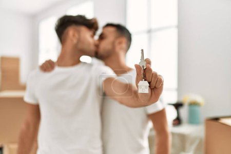 Foto de Dos hombres hispanos se besan y se abrazan sosteniendo la llave de una nueva casa en un nuevo hogar - Imagen libre de derechos