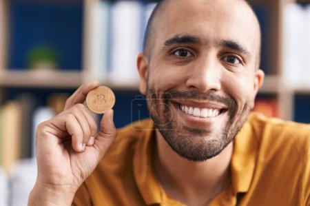 Foto de Hispanic man with beard holding virtual currency bitcoin looking positive and happy standing and smiling with a confident smile showing teeth - Imagen libre de derechos