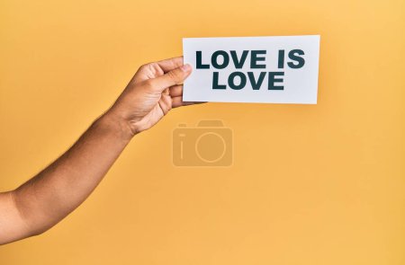 Téléchargez les photos : Hand of caucasian man holding paper with love is love message over isolated yellow background - en image libre de droit