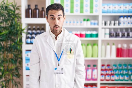 Téléchargez les photos : Bel homme hispanique travaillant à la pharmacie pharmacie peur et choqué avec surprise et expression étonnante, peur et visage excité. - en image libre de droit
