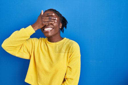 Photo for Beautiful black woman standing over blue background smiling and laughing with hand on face covering eyes for surprise. blind concept. - Royalty Free Image