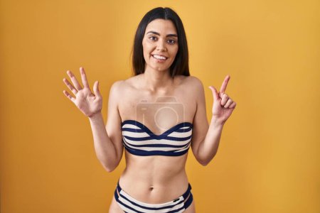 Téléchargez les photos : Young brunette woman wearing bikini over yellow background showing and pointing up with fingers number seven while smiling confident and happy. - en image libre de droit