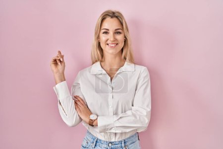Téléchargez les photos : Jeune femme caucasienne portant une chemise blanche décontractée sur fond rose avec un grand sourire sur le visage, pointant avec le doigt de la main sur le côté regardant la caméra. - en image libre de droit