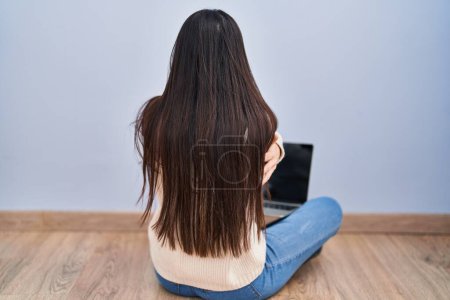 Foto de Mujer joven usando el ordenador portátil sentado en el suelo en casa abrazándose feliz y positivo desde atrás. amor propio y cuidado personal - Imagen libre de derechos