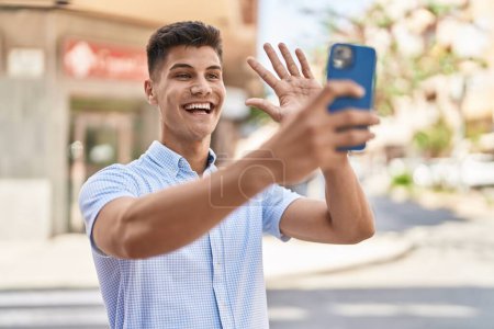 Foto de Joven hombre hispano sonriendo confiado teniendo videollamada en la calle - Imagen libre de derechos