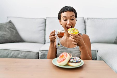 Téléchargez les photos : Jeune femme hispanique souriant confiant prendre le petit déjeuner à la maison - en image libre de droit