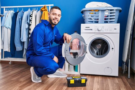 Foto de Hispanic repairman working on washing machine looking positive and happy standing and smiling with a confident smile showing teeth - Imagen libre de derechos