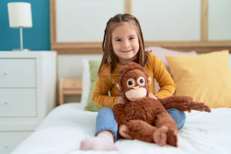 Photo for Adorable hispanic girl hugging monkey doll sitting on bed at bedroom - Royalty Free Image