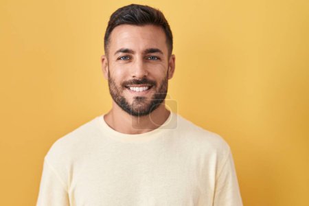 Foto de Hombre hispano guapo de pie sobre fondo amarillo con una sonrisa alegre y fresca en la cara. persona afortunada. - Imagen libre de derechos