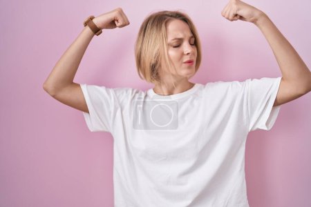 Photo for Young caucasian woman standing over pink background showing arms muscles smiling proud. fitness concept. - Royalty Free Image