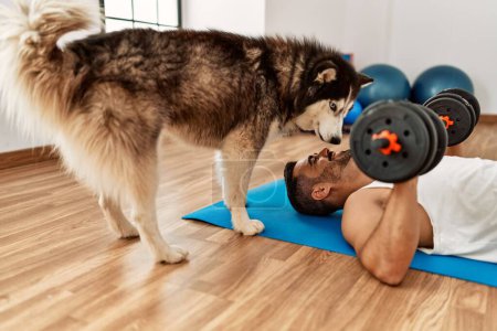 Photo for Young hispanic man smiling confident training using dumbbells with dog at sport center - Royalty Free Image