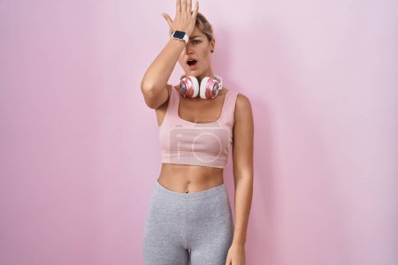 Téléchargez les photos : Young blonde woman wearing sportswear and headphones surprised with hand on head for mistake, remember error. forgot, bad memory concept. - en image libre de droit