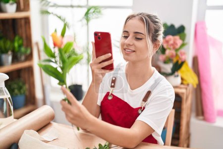 Photo for Young blonde woman florist make photo to flower by smartphone at flower shop - Royalty Free Image