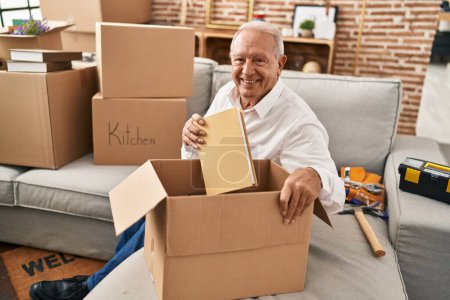 Téléchargez les photos : Senior homme souriant paquet de déballage confiant à la nouvelle maison - en image libre de droit
