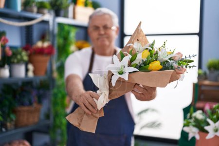 Téléchargez les photos : Homme moyen aux cheveux gris fleuriste tenant un bouquet de fleurs chez le fleuriste - en image libre de droit