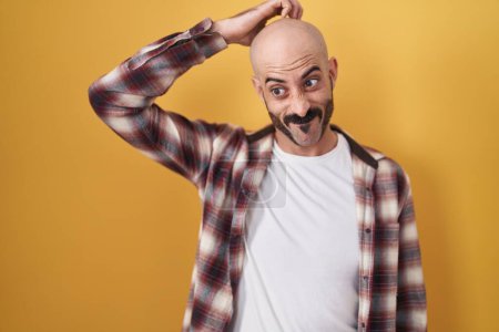Photo for Hispanic man with beard standing over yellow background confuse and wonder about question. uncertain with doubt, thinking with hand on head. pensive concept. - Royalty Free Image