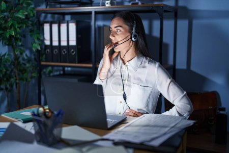 Photo for Young brunette woman wearing call center agent headset working late at night looking stressed and nervous with hands on mouth biting nails. anxiety problem. - Royalty Free Image