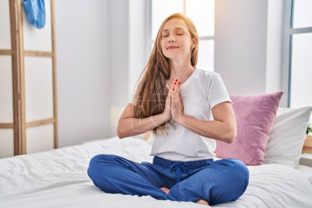 Photo for Young blonde woman doing yoga exercise sitting on bed at bedroom - Royalty Free Image