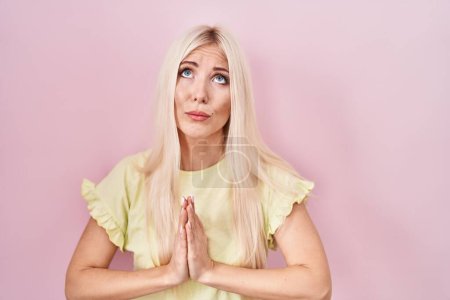 Téléchargez les photos : Caucasian woman standing over pink background begging and praying with hands together with hope expression on face very emotional and worried. begging. - en image libre de droit