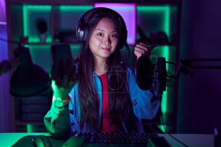 Photo for Young asian woman playing video games with smartphone pointing to the back behind with hand and thumbs up, smiling confident - Royalty Free Image