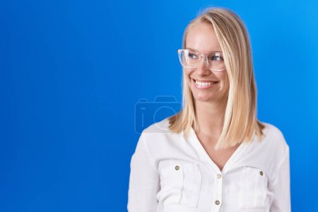 Photo for Young caucasian woman standing over blue background looking away to side with smile on face, natural expression. laughing confident. - Royalty Free Image