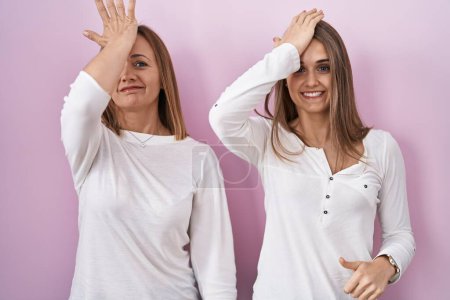 Téléchargez les photos : Middle age mother and young daughter standing over pink background surprised with hand on head for mistake, remember error. forgot, bad memory concept. - en image libre de droit