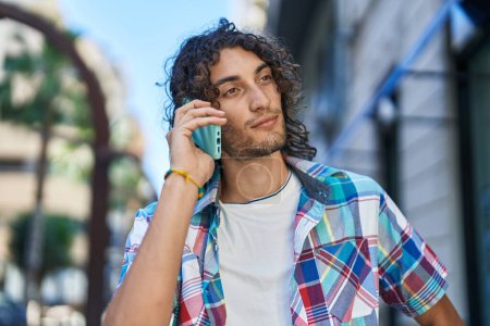 Photo for Young hispanic man talking on smartphone with serious expression at street - Royalty Free Image