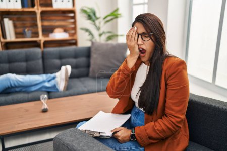 Foto de Young hispanic woman working as psychology counselor yawning tired covering half face, eye and mouth with hand. face hurts in pain. - Imagen libre de derechos