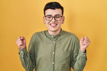 Foto de Non binary person standing over yellow background excited for success with arms raised and eyes closed celebrating victory smiling. winner concept. - Imagen libre de derechos