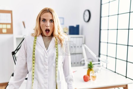 Foto de Beautiful blonde nutritionist woman at dietitian clinic scared and amazed with open mouth for surprise, disbelief face - Imagen libre de derechos