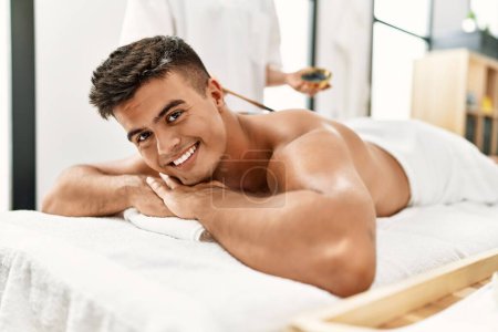 Foto de Young hispanic man smiling confident having skin back treatment at beauty center - Imagen libre de derechos