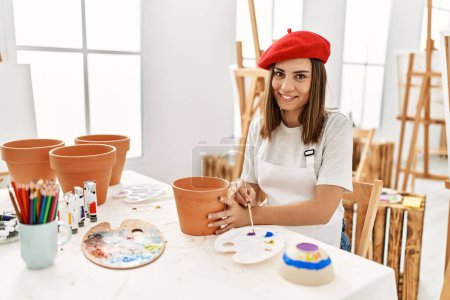 Foto de Joven artista hispana con boina francesa sosteniendo olla de barro en el estudio de arte. - Imagen libre de derechos