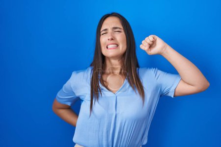 Photo for Young brunette woman standing over blue background stretching back, tired and relaxed, sleepy and yawning for early morning - Royalty Free Image