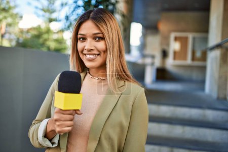 Téléchargez les photos : Jeune femme latine souriant confiant en utilisant le microphone à la rue - en image libre de droit