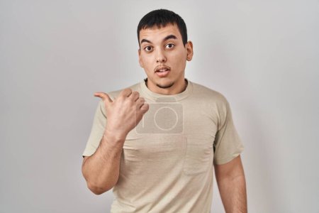 Foto de Hombre árabe joven con camiseta casual sorprendido señalando con el dedo de la mano a un lado, boca abierta expresión asombrada. - Imagen libre de derechos