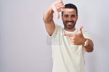 Foto de Hispanic man with beard standing over isolated background smiling making frame with hands and fingers with happy face. creativity and photography concept. - Imagen libre de derechos