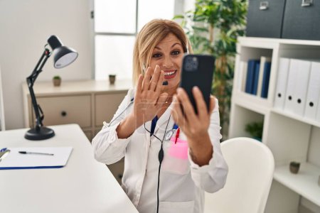 Foto de Middle age blonde woman wearing doctor uniform having medical teleconsultation at clinic - Imagen libre de derechos