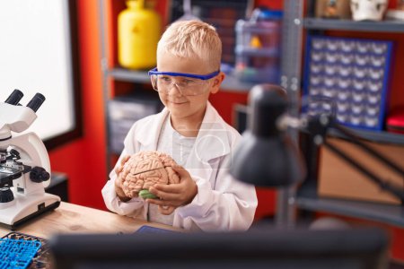 Foto de Adorable niño científico sonriendo confiado sosteniendo el cerebro en el aula - Imagen libre de derechos