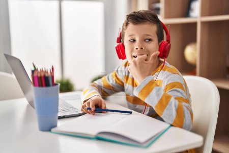 Foto de Young caucasian kid doing homework at home pointing thumb up to the side smiling happy with open mouth - Imagen libre de derechos