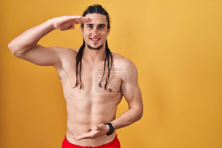 Téléchargez les photos : Hispanic man with long hair standing shirtless over yellow background gesturing with hands showing big and large size sign, measure symbol. smiling looking at the camera. measuring concept. - en image libre de droit