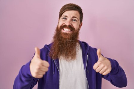 Téléchargez les photos : Homme caucasien avec une longue barbe debout sur fond rose signe de succès faisant geste positif avec la main, pouces levés souriant et heureux. expression joyeuse et geste gagnant. - en image libre de droit