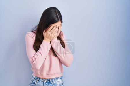 Photo for Young brunette woman standing over blue background with sad expression covering face with hands while crying. depression concept. - Royalty Free Image