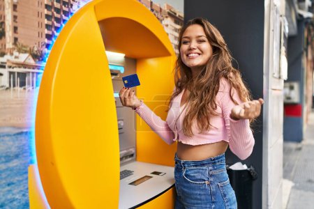 Photo for Young hispanic woman taking cash from atm with credit card screaming proud, celebrating victory and success very excited with raised arm - Royalty Free Image
