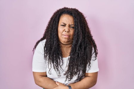 Téléchargez les photos : Plus size hispanic woman standing over pink background with hand on stomach because indigestion, painful illness feeling unwell. ache concept. - en image libre de droit