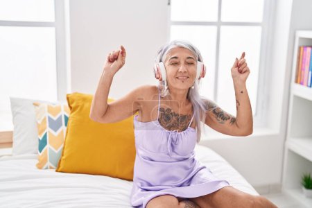 Téléchargez les photos : Femme aux cheveux gris du Moyen Âge dansant et écoutant de la musique allongée sur le lit dans la chambre - en image libre de droit